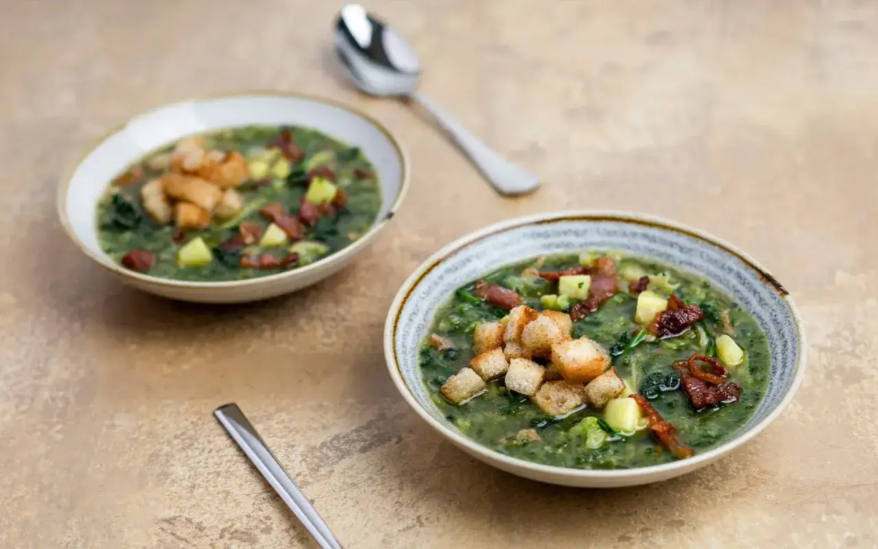 Due ciotole di zuppa di cavolo nero, guarnite con crostini e pancetta croccante, pronte per essere gustate.