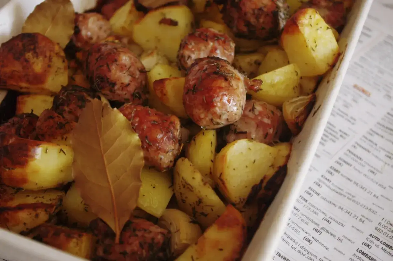 Pyszna kiełbasa z piekarnika z ziemniakami i liśćmi laurowymi, pieczona do złotego koloru.