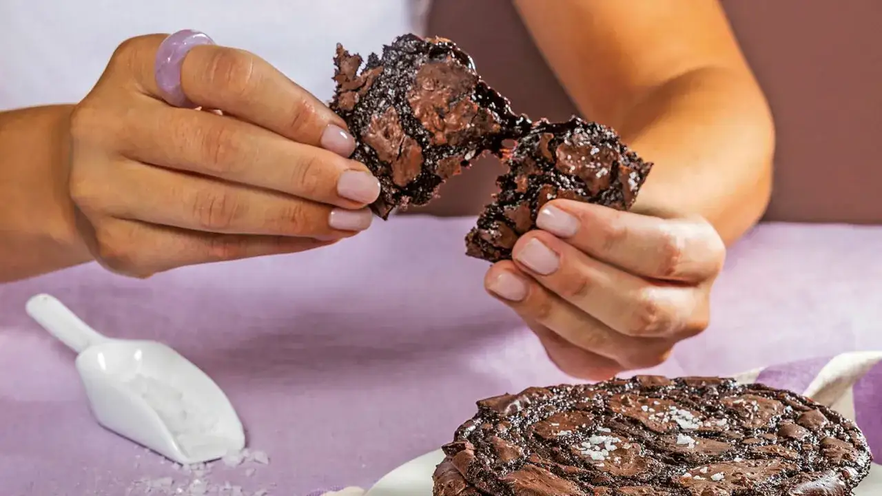 H&auml;nderna bryter is&auml;r en seg chocolate chip cookie, med en hel cookie och en skopa salt i bakgrunden.