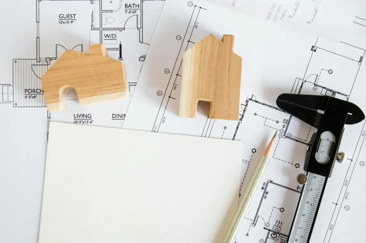Dwa drewniane domki na planach architektonicznych, ołówek i suwmiarka. Czy świadectwo energetyczne będzie wymagane dla altan na działkach ROD?