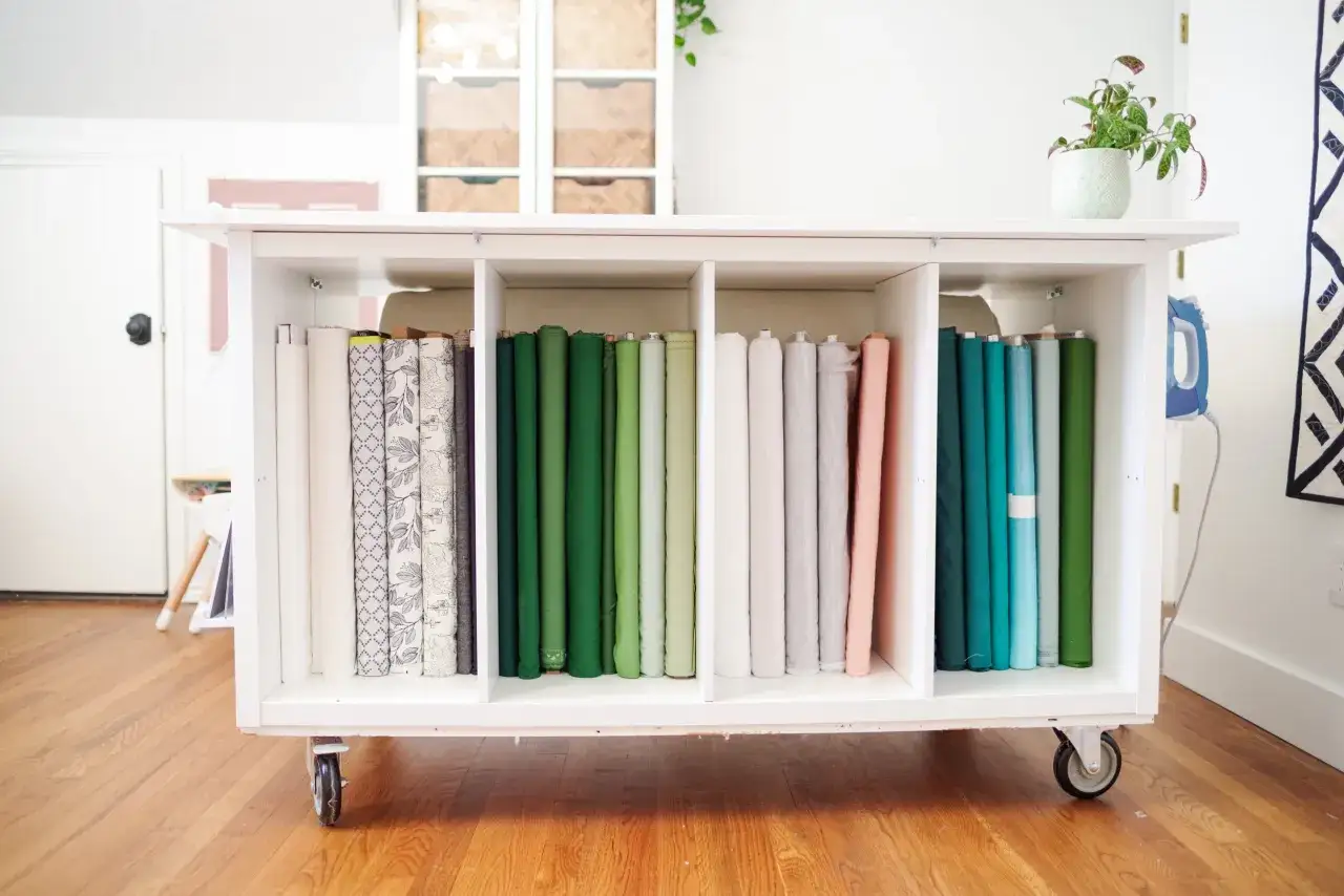 A white rolling cart displays neatly organized rolls of fabric, perfect for cut and sew knits.