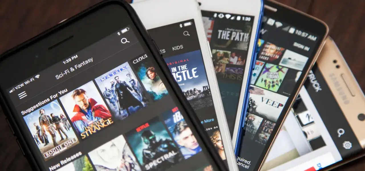 Kilka smartfonów wyświetla **aplikacje do oglądania filmów**, pokazując okładki tytułów takich jak 