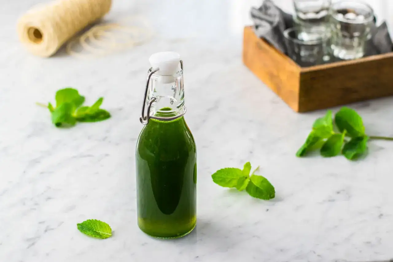 Bottiglia di sciroppo di menta fatto in casa, con foglie di menta fresca sparse sul piano di marmo.