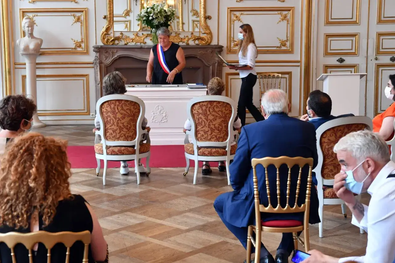 C&eacute;r&eacute;monie de mariage &agrave; Strasbourg. Une officiante, portant une &eacute;charpe tricolore, pr&eacute;side la c&eacute;r&eacute;monie. Des invit&eacute;s masqu&eacute;s sont assis, attendant le moment de la signature.