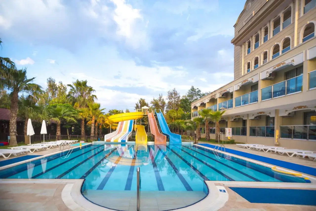 Erfrischender Pool mit Wasserrutschen im Arum Barut Collection Resort. Palmen und ein Hotelgebäude säumen die Anlage.