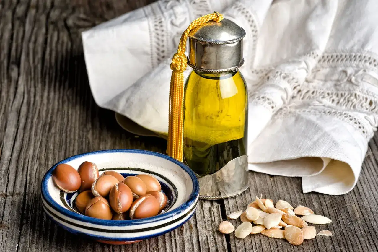 Bouteille d'huile d'argan dor&eacute;e, amandes d'argan dans un bol, et amandes d&eacute;cortiqu&eacute;es sur fond de bois.