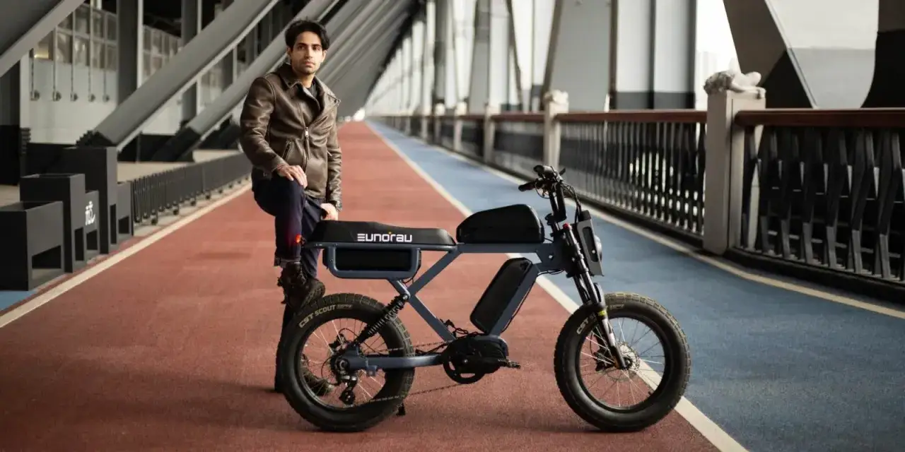 Młody mężczyzna w sk&oacute;rzanej kurtce opiera się o stylowy rower elektryczny. Ten model, z imponującym zasięgiem 300 km, idealnie sprawdzi się na długie wyprawy.