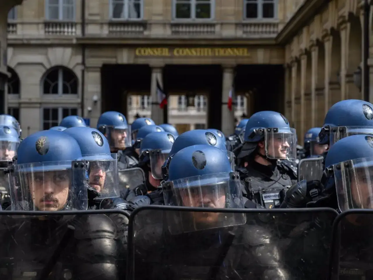 Un grupo de gendarmes con cascos azules y escudos protectores se preparan frente a un edificio con la inscripci&oacute;n 