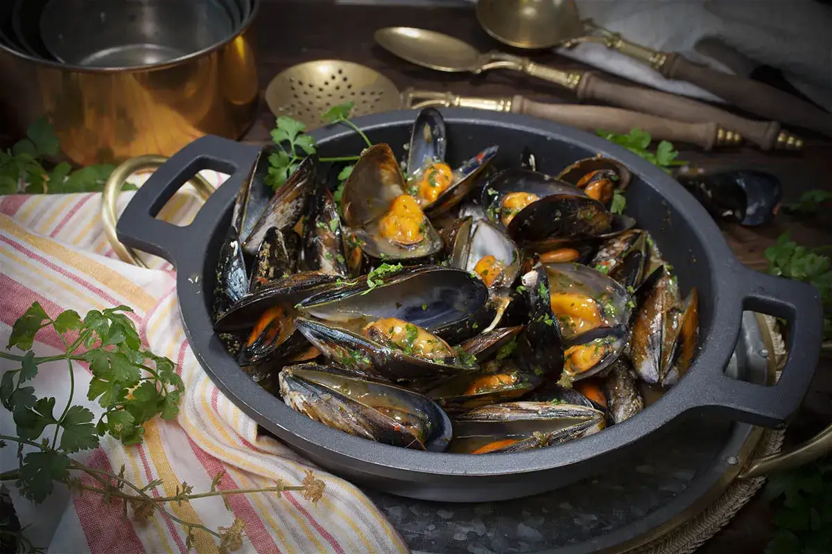 Mejillones a la gallega reci&eacute;n cocinados, servidos en una cazuela con perejil fresco.