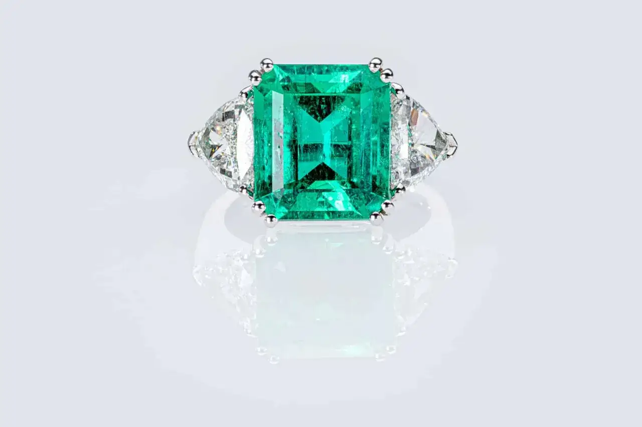 Anello con smeraldo centrale a taglio rettangolare, affiancato da due diamanti a taglio triangolare. L'incastonato significato di questo gioiello è pura eleganza.