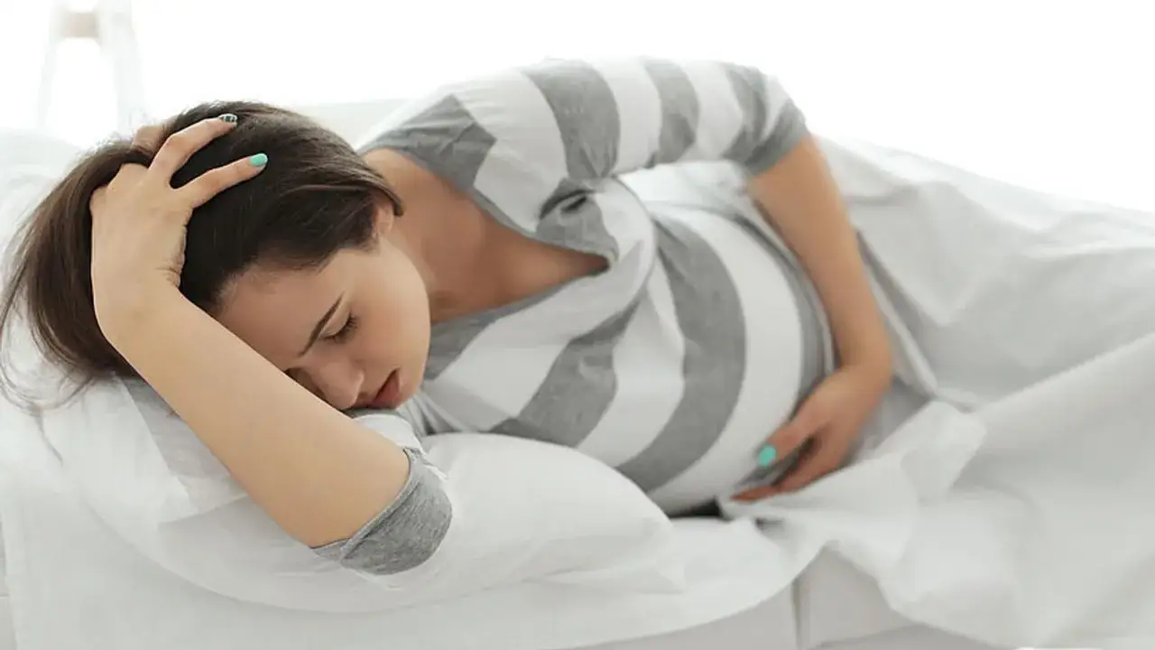 Schwangere Frau liegt im Bett, h&auml;lt sich den Kopf und sp&uuml;rt die ersten Wehen.