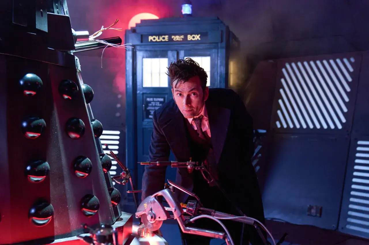 L'acteur David Tennant, dans son rôle du Docteur, manipule un appareil devant le Tardis, à côté d'un Dalek.