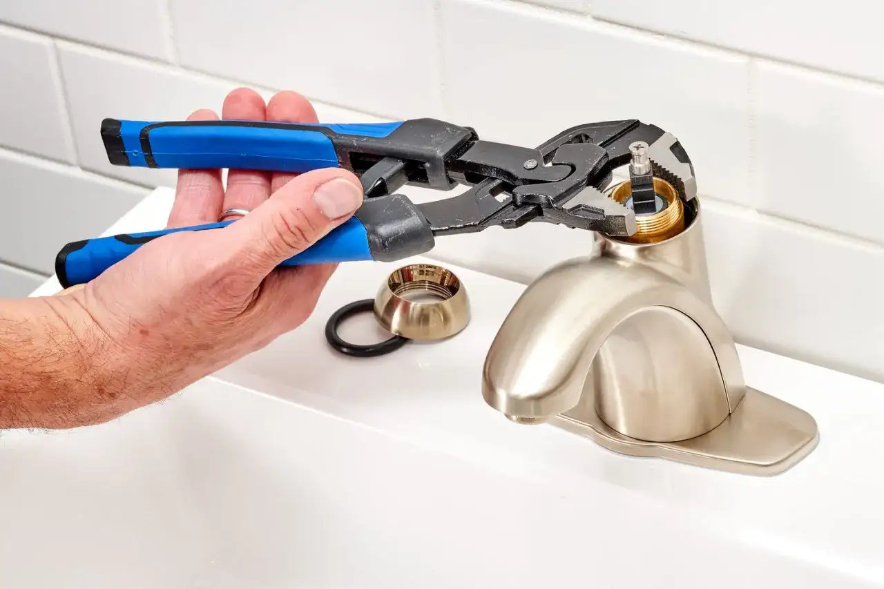 A hand uses pliers to remove a faucet cartridge, demonstrating how to replace faucet cartridge parts.