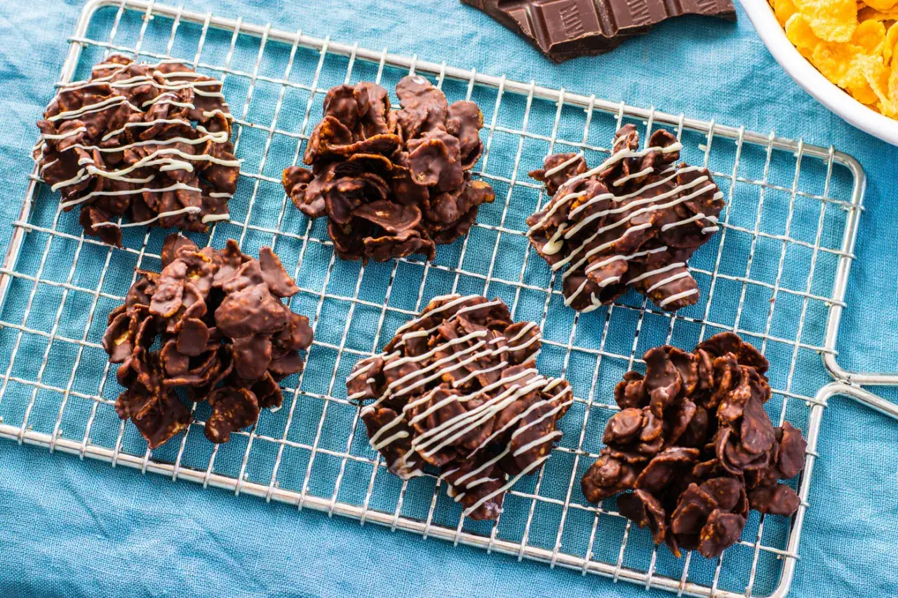 Sei dolciose rose del deserto al cioccolato, alcune decorate con glassa bianca, riposano su una griglia.