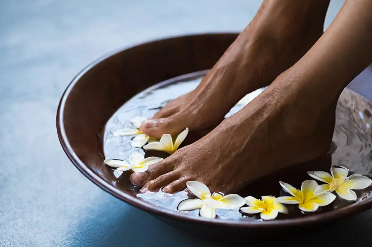 Soaking feet in a warm bath with Epsom salt and frangipani flowers for soothing foot pain.