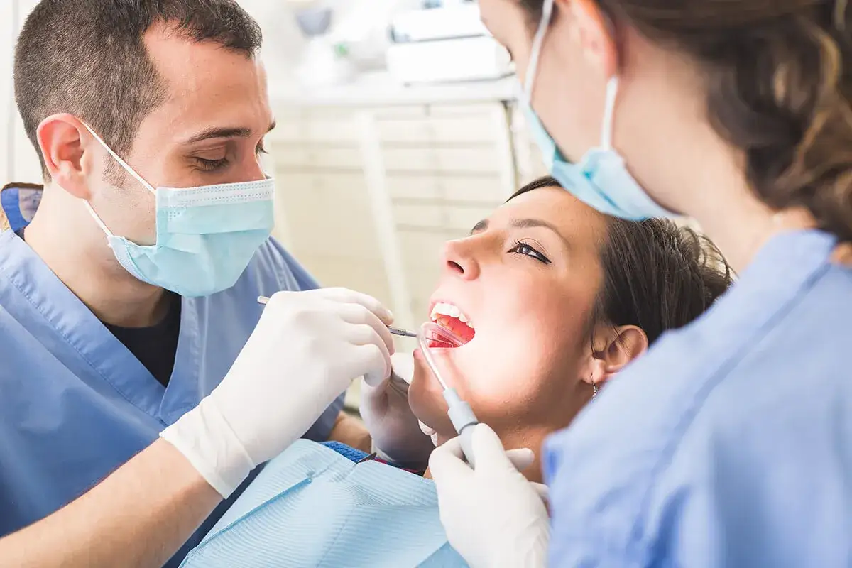 Dentysta i asystentka przeprowadzają zabieg usuwania ósemek. Pacjentka ma otwarte usta, a lekarz używa narzędzi.