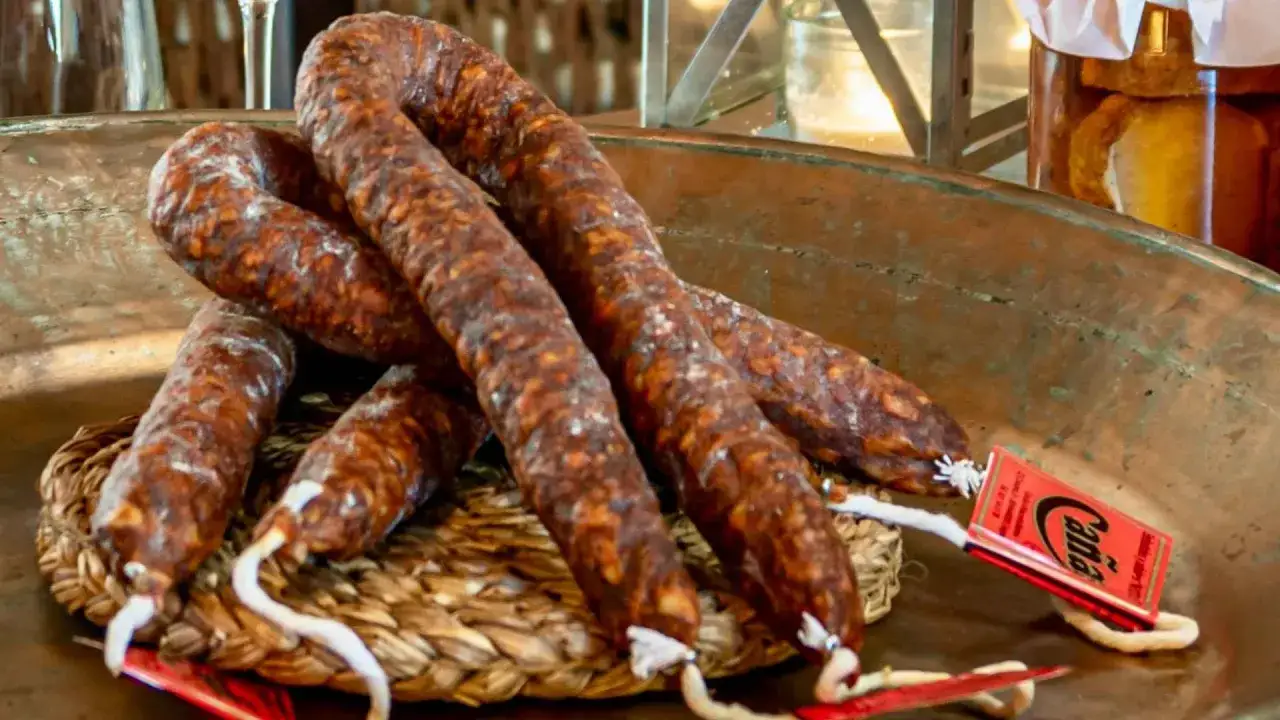 Varios chorizos curados, con aspecto de estar en mal estado, reposan sobre una cesta de mimbre en un cuenco de cobre.