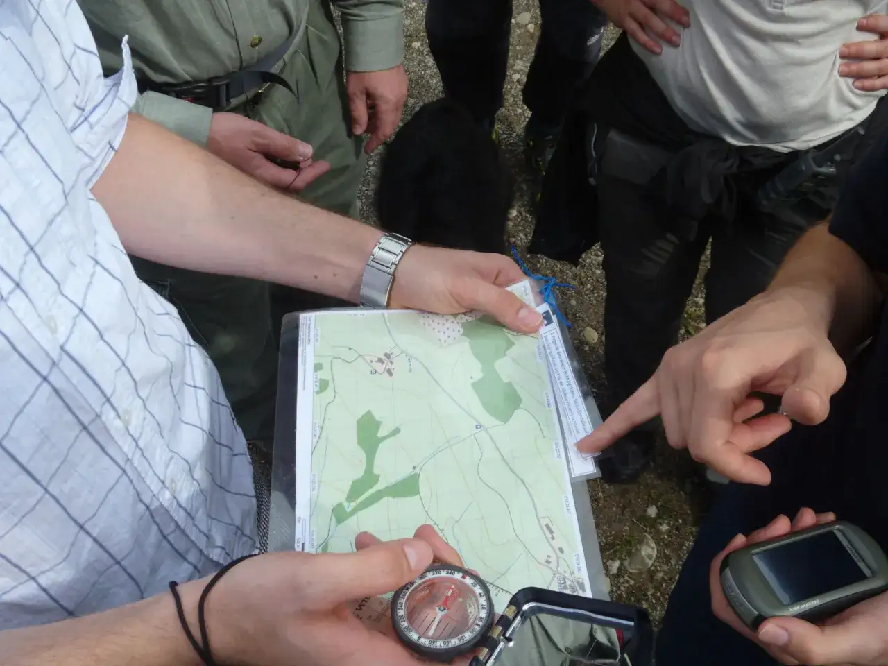 Hände halten Karte und Kompass, planen die nächste Etappe eines adventure racing. Ein GPS-Gerät liegt bereit.