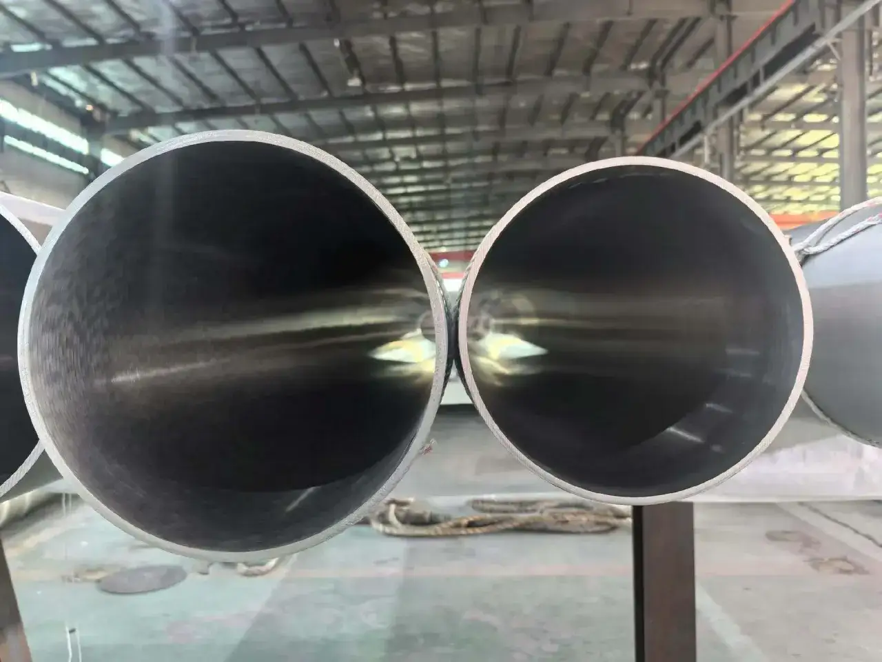 Deux tubes en acier inoxydable 304l brillants, vus de l'intérieur, dans un entrepôt.