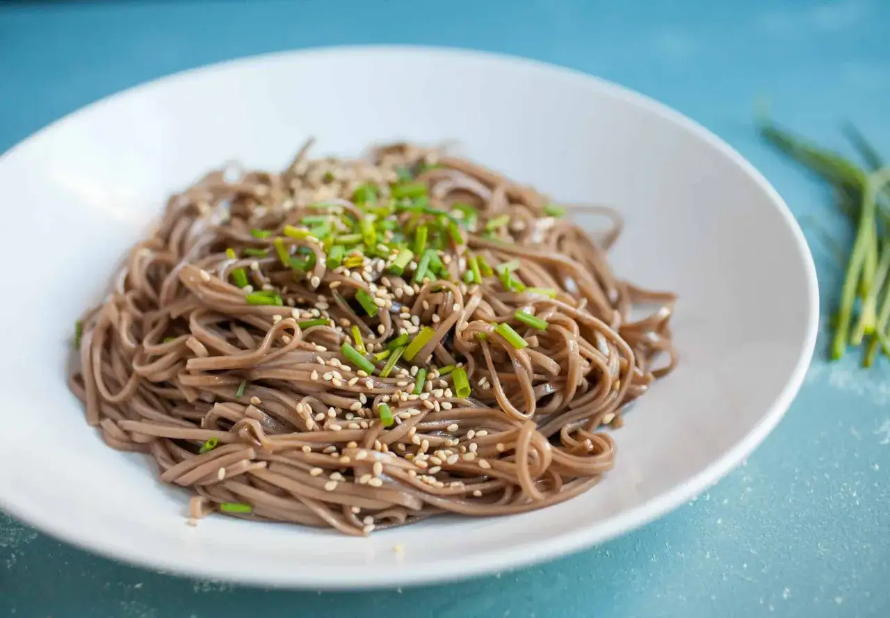 Prosty makaron soba przepis: pyszne danie z sezamem i szczypiorkiem na białym talerzu.