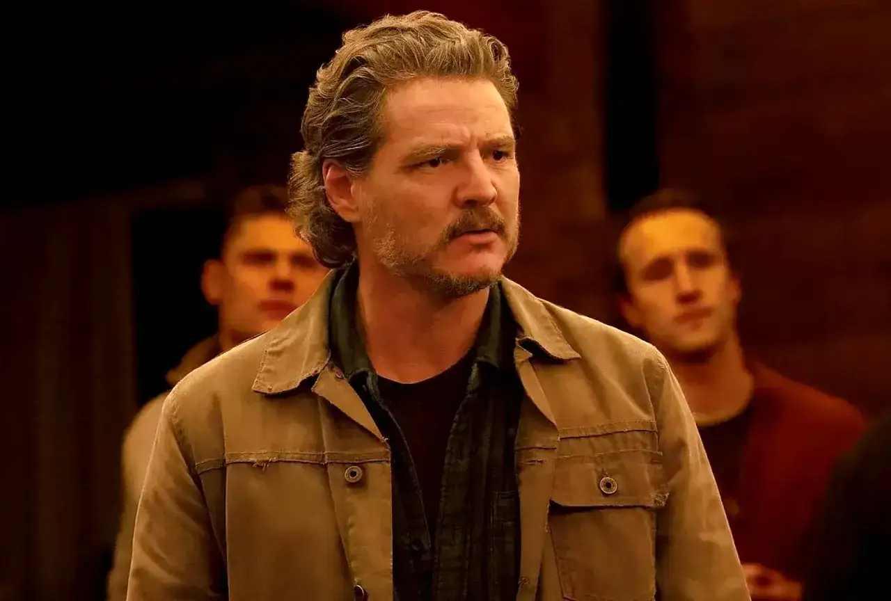 Joel Miller, con su característica barba y cabello revuelto, mira con seriedad mientras otros hombres se vislumbran al fondo.