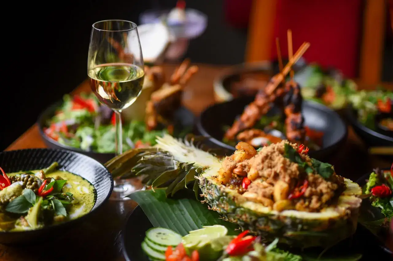 Ett glas vitt vin till thaimat. En festmåltid med grön curry, ananas fylld med kött och grillspett.