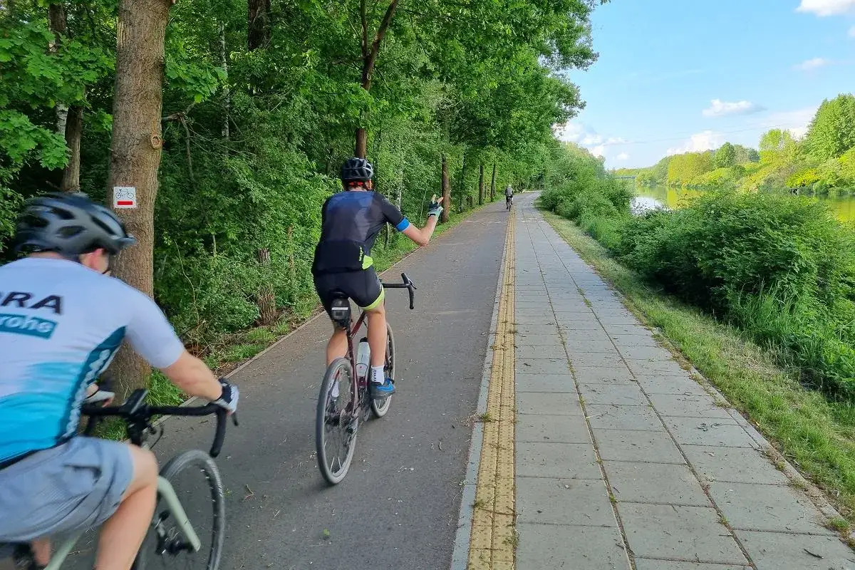 Rowerzyści na malowniczej trasie rowerowej Warszawa, wzdłuż zielonych drzew i rzeki.