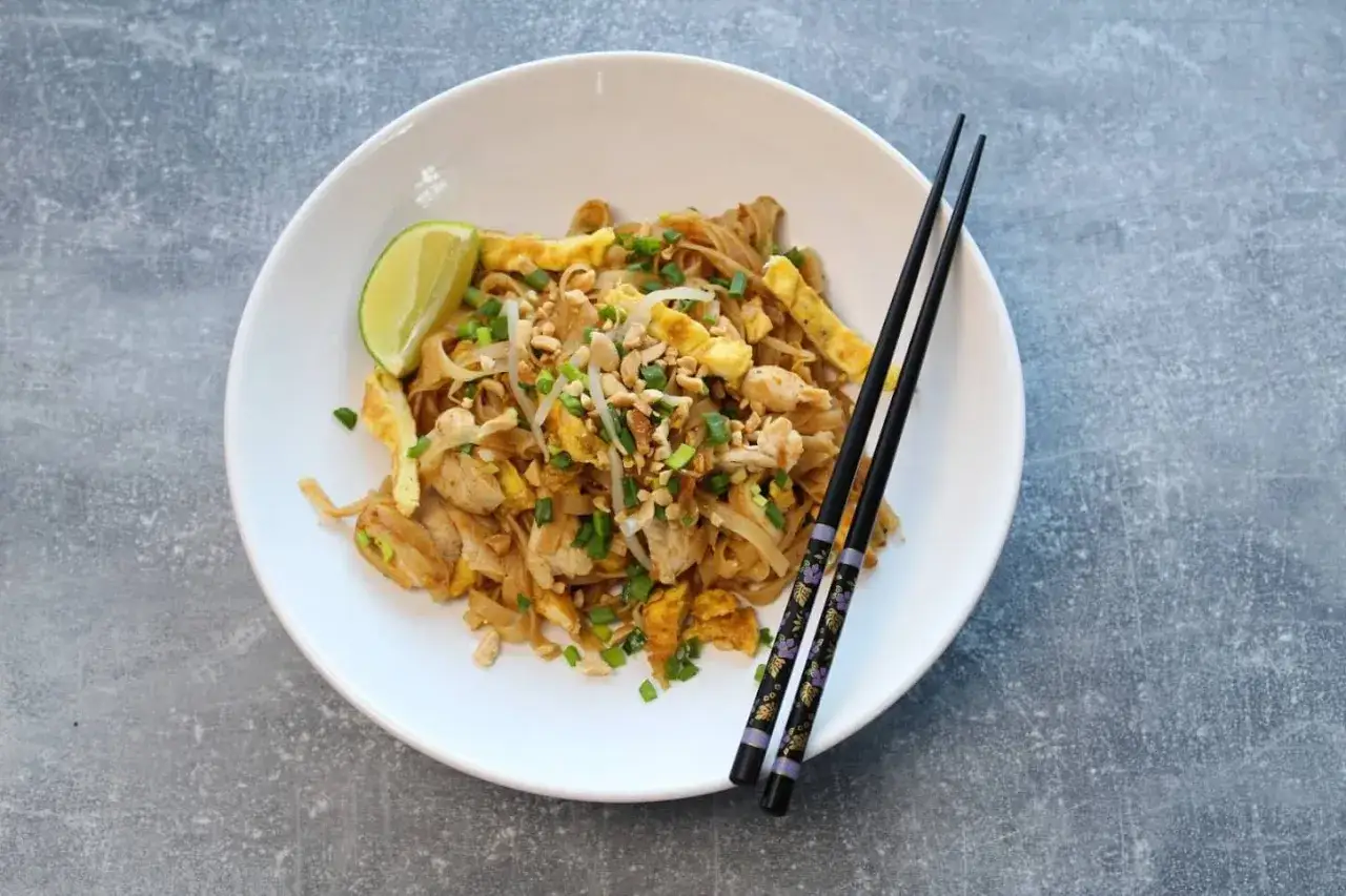 Pyszny pad thai z kurczakiem, jajkiem i orzeszkami ziemnymi, podany z limonką i pałeczkami. Idealny sos pad thai.