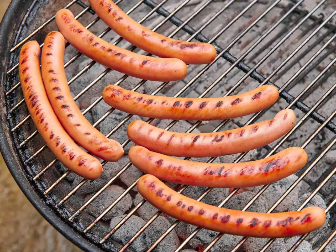 Plusieurs saucisses dorées et grillées sur un barbecue, prêtes pour un hot dog parfait.