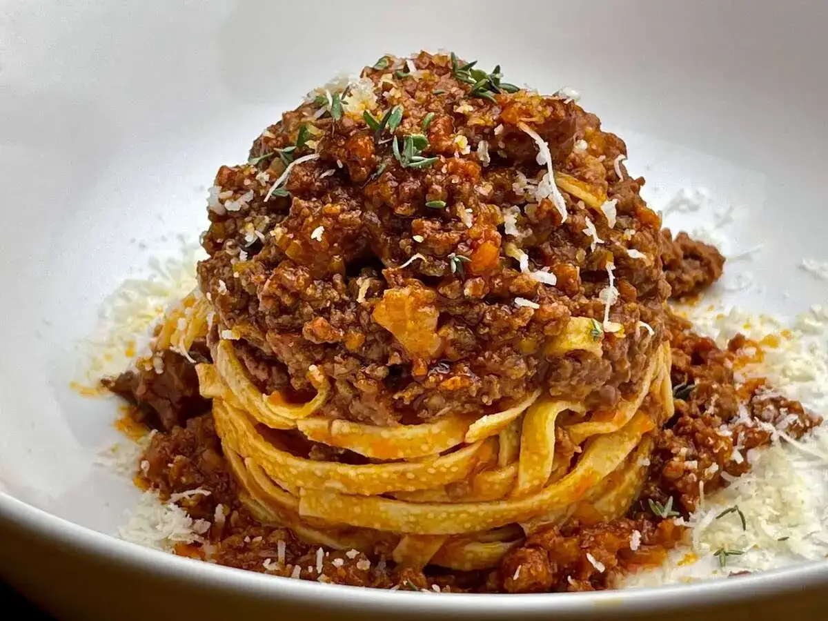 Ein Turm aus Tagliatelle, bedeckt mit einem herzhaften Sos Bolognese und bestreut mit Parmesan und Kräutern.