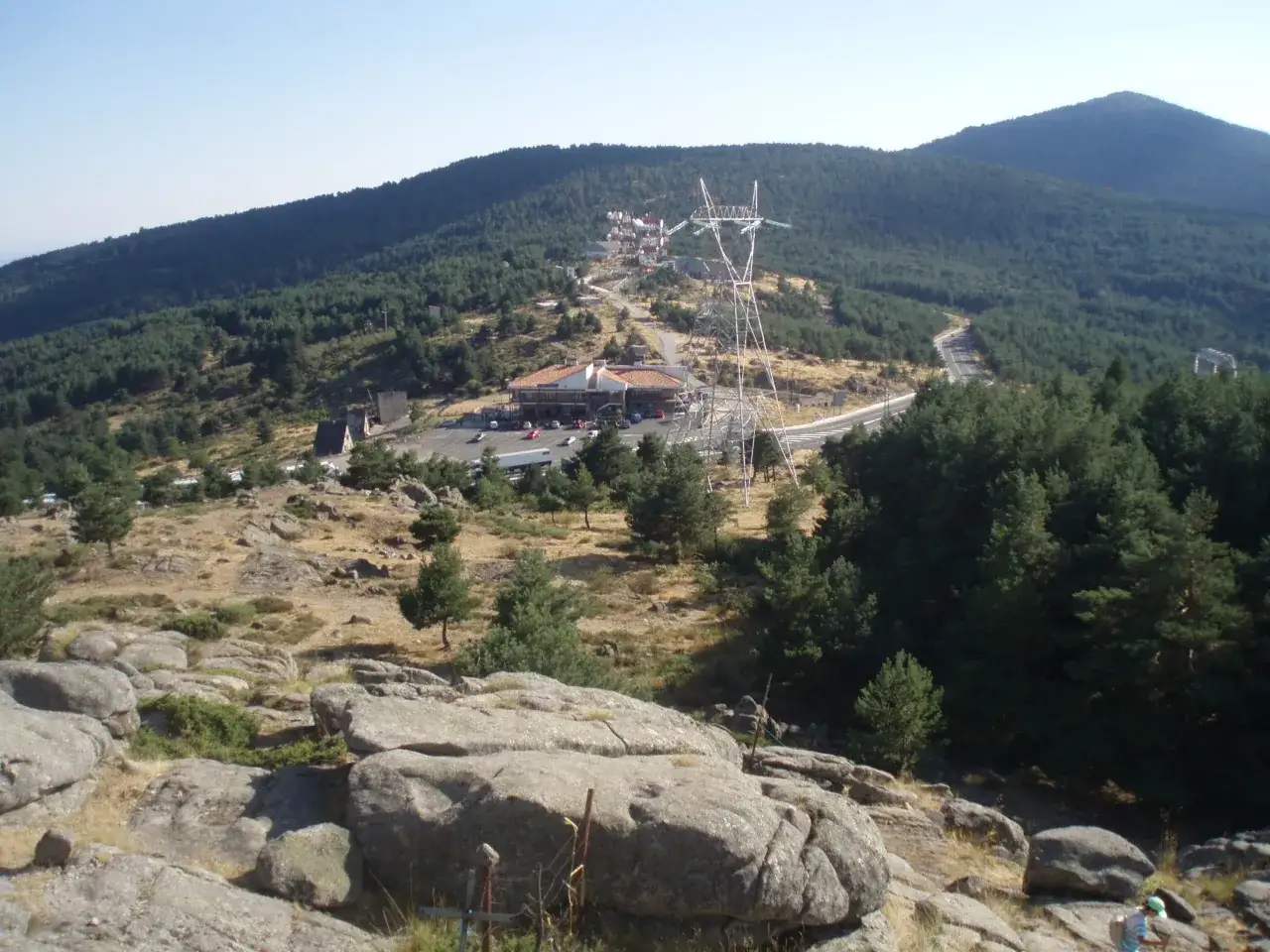 Vista panor&aacute;mica de un paso de monta&ntilde;a con un restaurante, una torre el&eacute;ctrica y un camino serpenteante entre pinos.