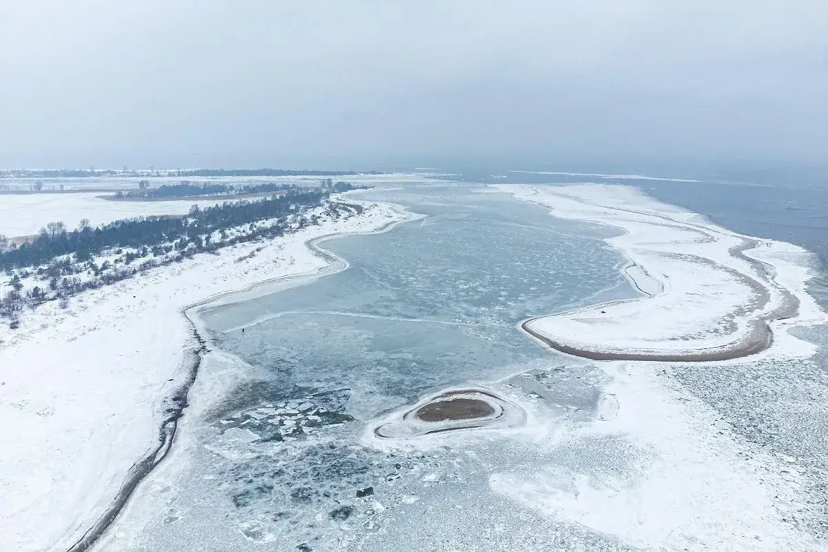 Mikoszewo zimą. Lodowe góry na zamarzniętej wodzie, śnieg i drzewa tworzą zimowy krajobraz.