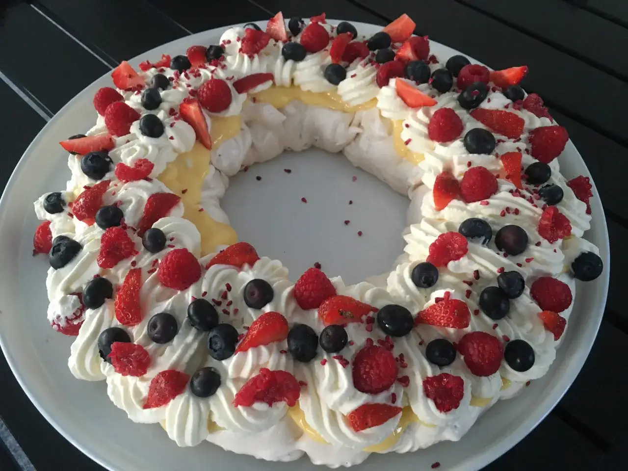 En vacker kransformad pavlova med fluffig grädde, färska bär och en härlig lemoncurd. Perfekt för sommarens firanden!