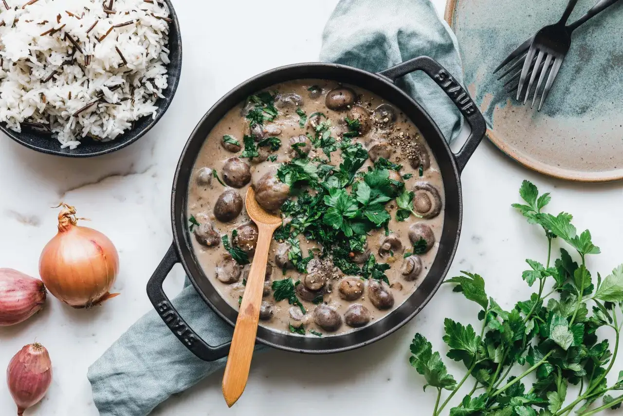 Cremige Rahmchampignons in einer gusseisernen Pfanne, garniert mit Petersilie. Dazu wilder Reis. Ein köstliches Rahmchampignons Rezept.