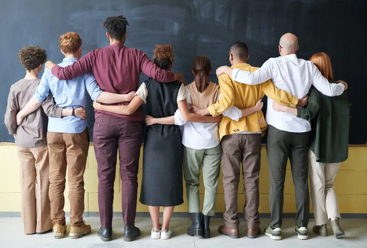 Un gruppo di persone abbracciate davanti a una lavagna, un'immagine che cattura la **social definizione** di unit&agrave; e supporto reciproco.
