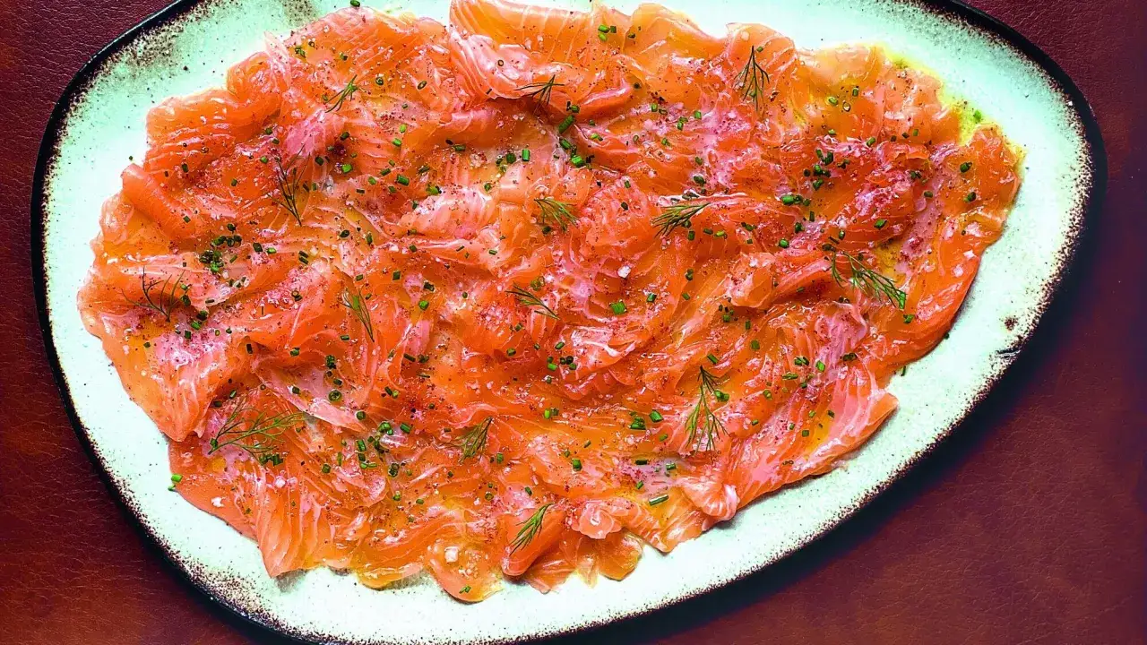 D&eacute;licieux carpaccio de saumon finement tranch&eacute;, parsem&eacute; d'herbes fra&icirc;ches et d'&eacute;pices sur une assiette claire.