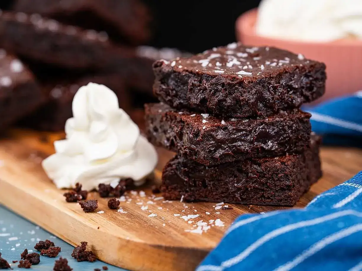 Färska bitar av brownie i långpanna, toppade med flingsalt och serverade med vispad grädde. En härlig chokladupplevelse!