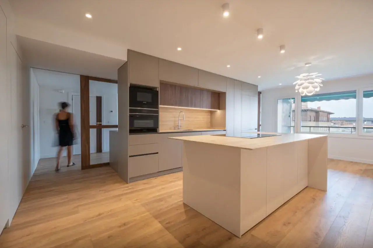 Cocina moderna con isla central, electrodom&eacute;sticos integrados y suelo de madera. Un ejemplo de los **estudios de arquitectura** que crean espacios funcionales y elegantes.