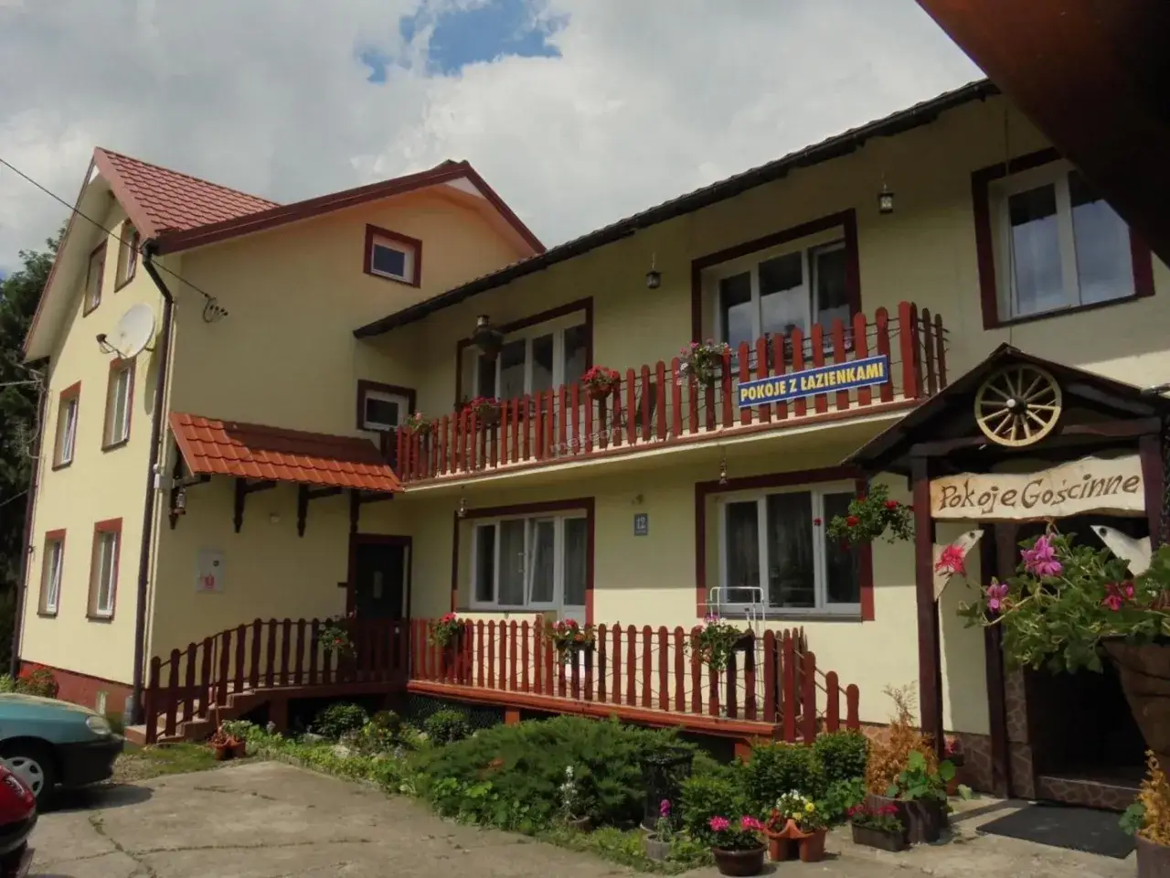 Pokój gościnny w Korczowej. Żółty dom z czerwonymi elementami, balustradami i kwitnącymi kwiatami.
