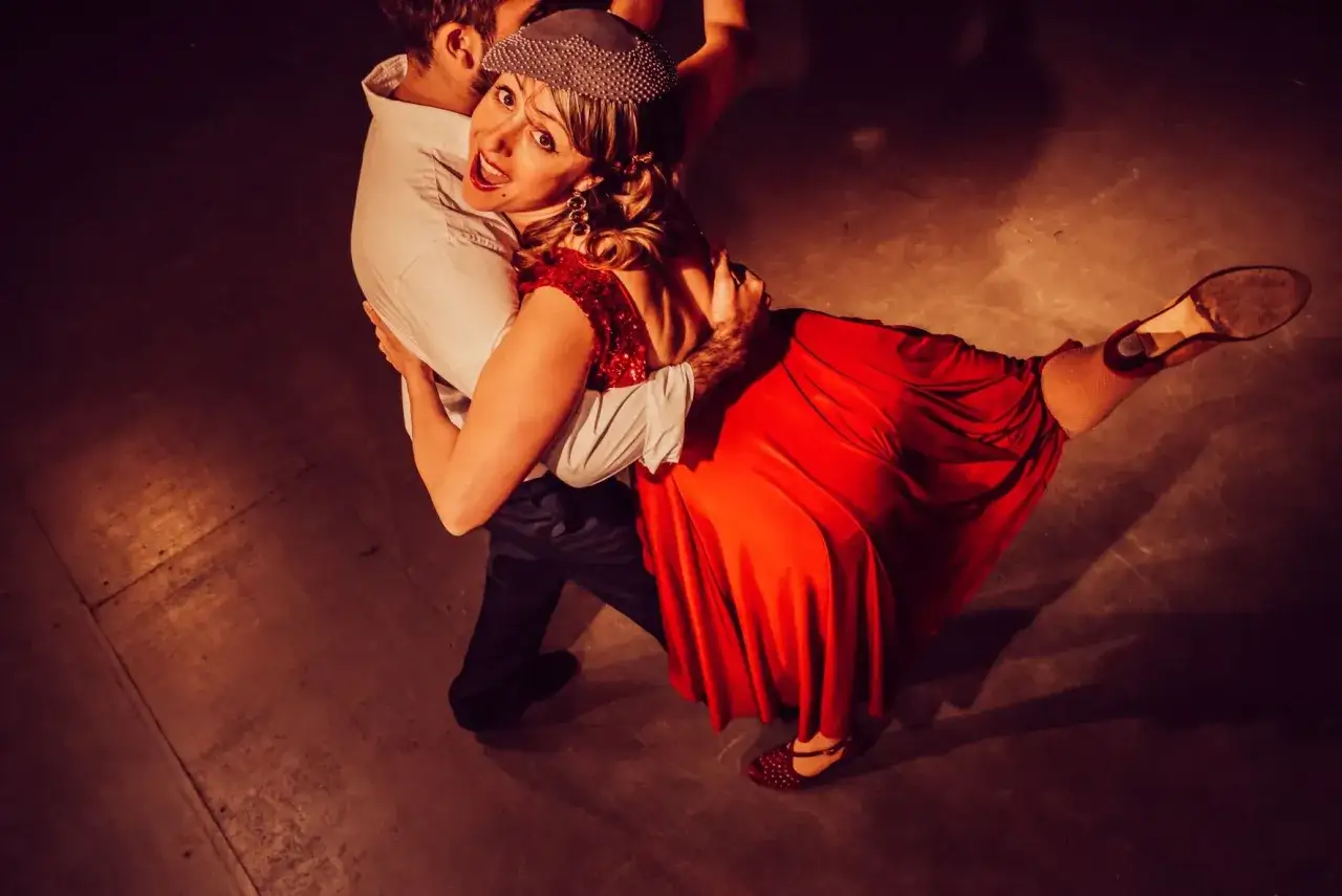 Para tańczy tango. Kobieta w czerwonej sukni i mężczyzna w białej koszuli wykonują dynamiczny sway.