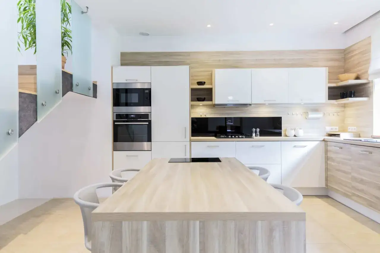 Cocinas modernas con isla central de madera clara y gabinetes blancos. Los colores neutros y la iluminación crean un ambiente elegante.