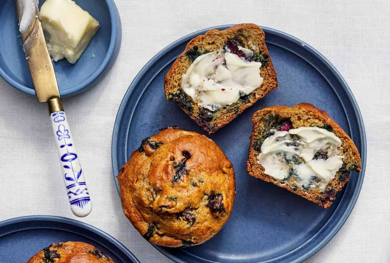 Leckere protein muffins rezept mit Blaubeeren, aufgeschnitten und mit Butter bestrichen, auf blauem Teller.