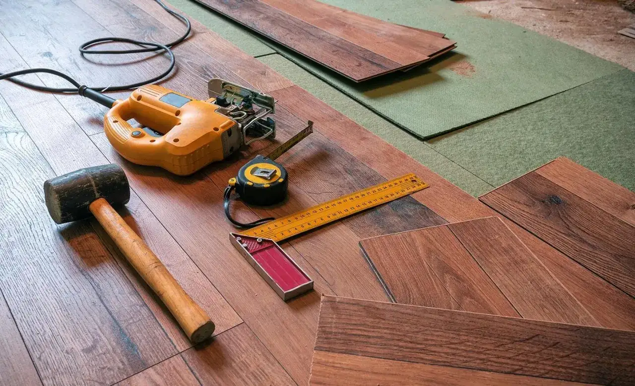 Tools for how to install click lock flooring: jigsaw, rubber mallet, tape measure, and square on wood planks and underlayment.
