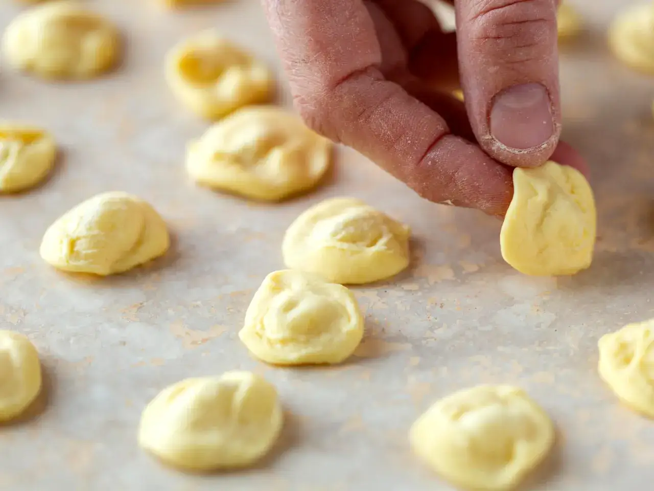 Main d'une personne fa&ccedil;onnant des orecchiette, une recette traditionnelle italienne, sur une surface claire.