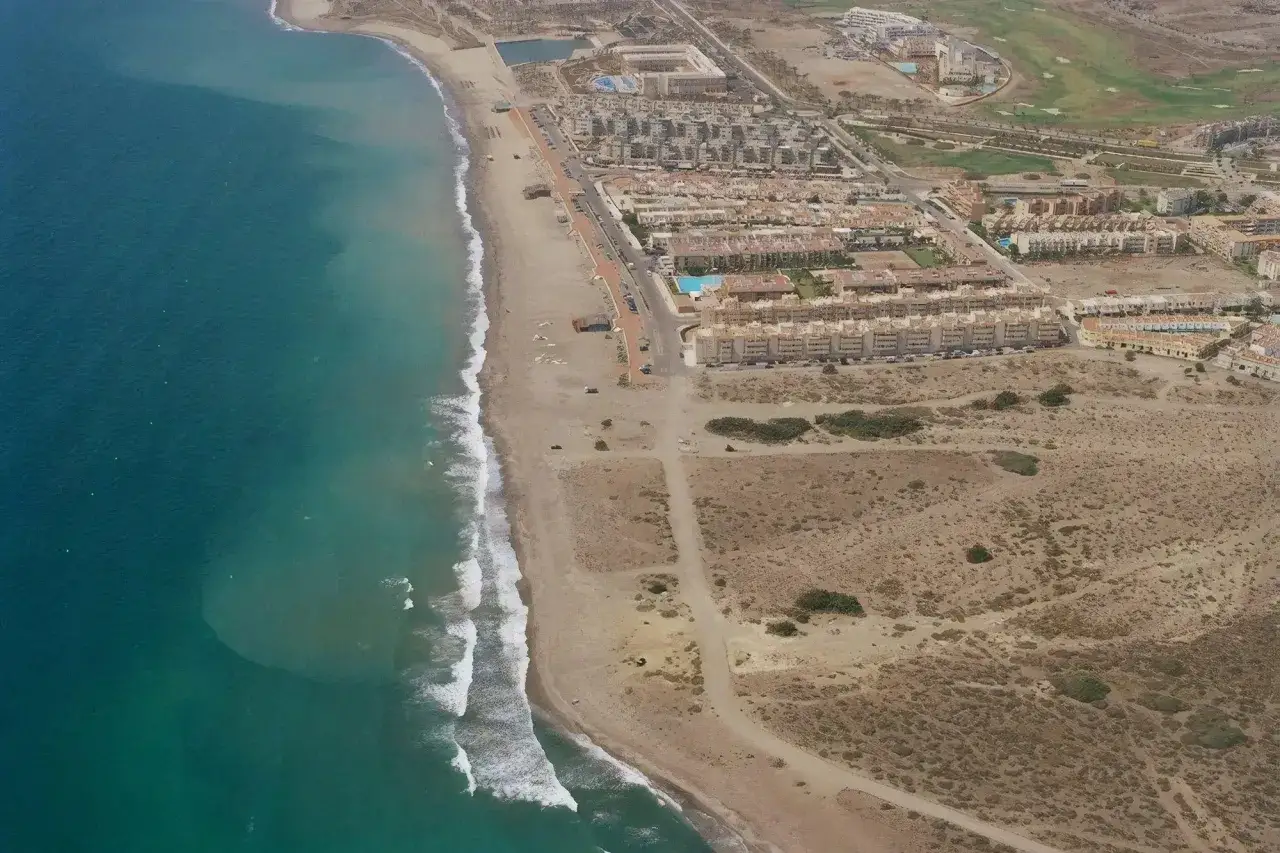 Vista aérea de la playa del Retamar, con el mar turquesa, arena dorada, urbanizaciones y un campo de golf.
