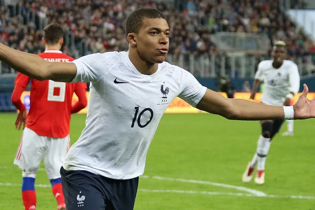 Kylian Mbappé w białej koszulce z numerem 10, świętuje bramkę. Jego waga i siła pozwalają mu na dynamiczne akcje na boisku.