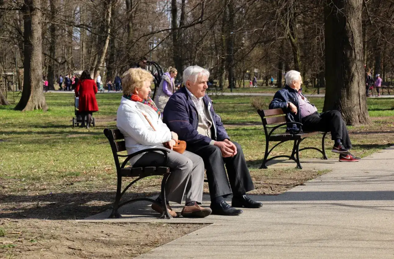Seniorzy na ławce w parku, cieszący się spokojem. To świetny przykład, co robić na emeryturze: relaks na świeżym powietrzu.