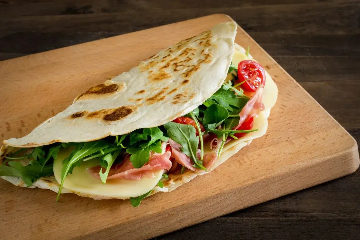 Piadina ripiena con prosciutto, formaggio, rucola e pomodorini. Una ricetta piadina veloce e gustosa, perfetta per un pasto informale.