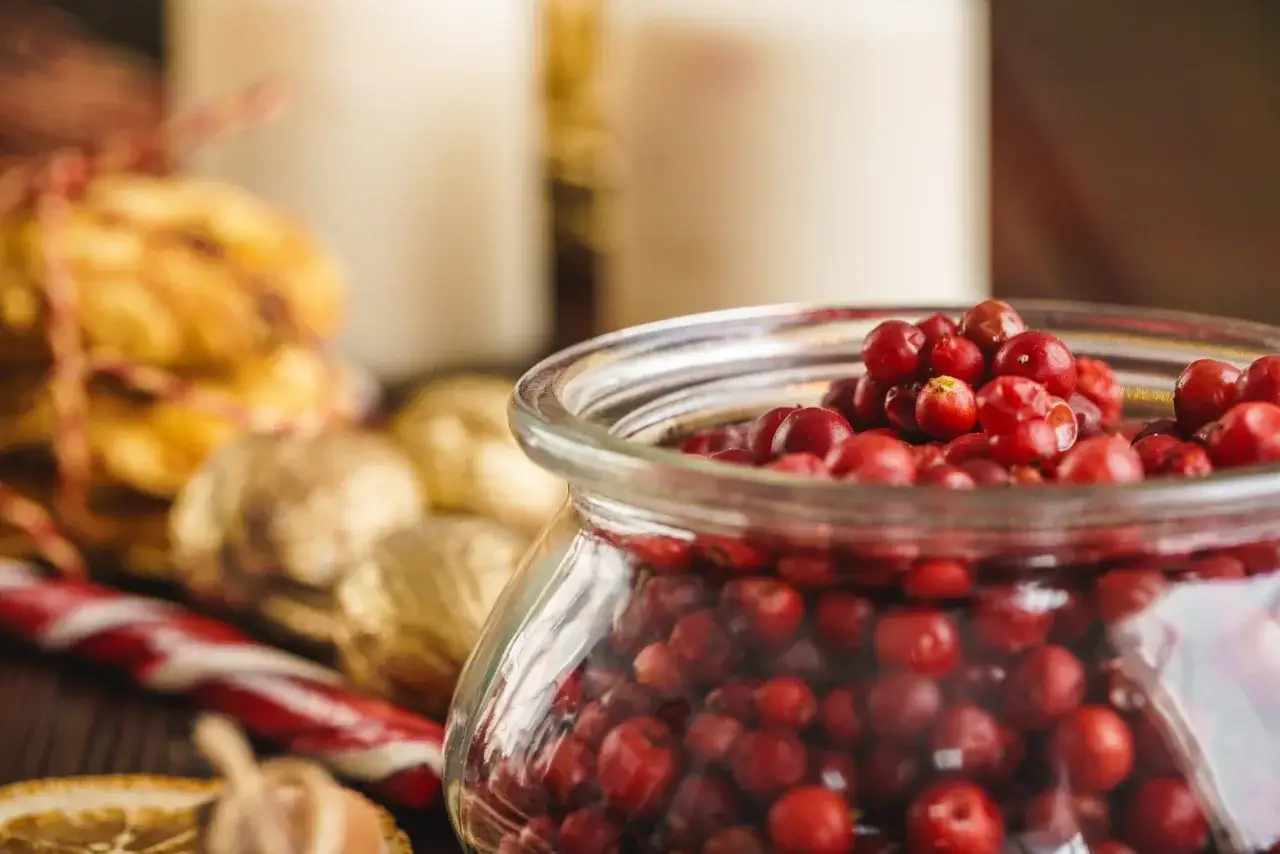 Słoik pełen żurawiny, która ma wiele cennych właściwości. Obok ciasteczka i ozdoby świąteczne.