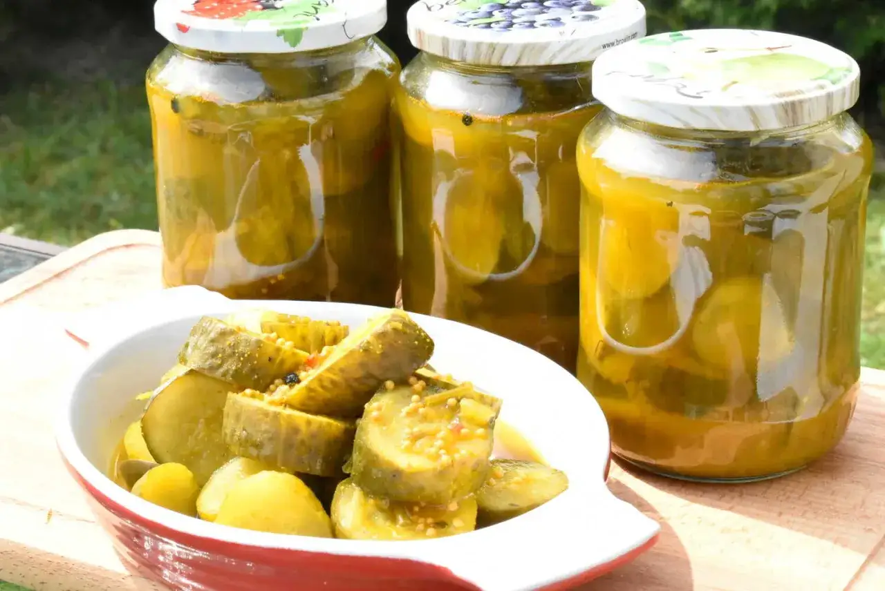 Słoiki z ogórkami w curry ze skórką, obok miseczka z pokrojonymi ogórkami.